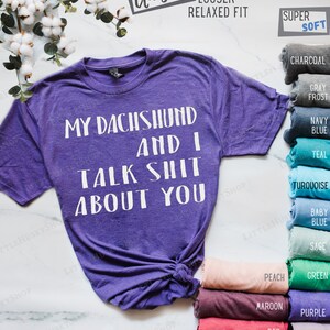 Puede incluir: Camiseta unisex de color morado con el texto "My Dachshund and I Talk Shit About You" en blanco. La camiseta est&aacute; disponible en una variedad de colores, incluyendo carb&oacute;n, gris escarcha, azul marino, azul aguamarina, turquesa, azul beb&eacute;, salvia, verde, melocot&oacute;n, granate, rojo, azul real, morado y lavanda.