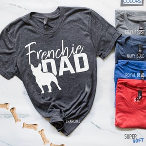 May include: Charcoal gray unisex V-neck t-shirt with the text "Frenchie DAD" and a white French Bulldog silhouette. Additional color options include Gray Frost, Navy Blue, Royal Blue, and Red. The shirt is labeled as Super Soft.