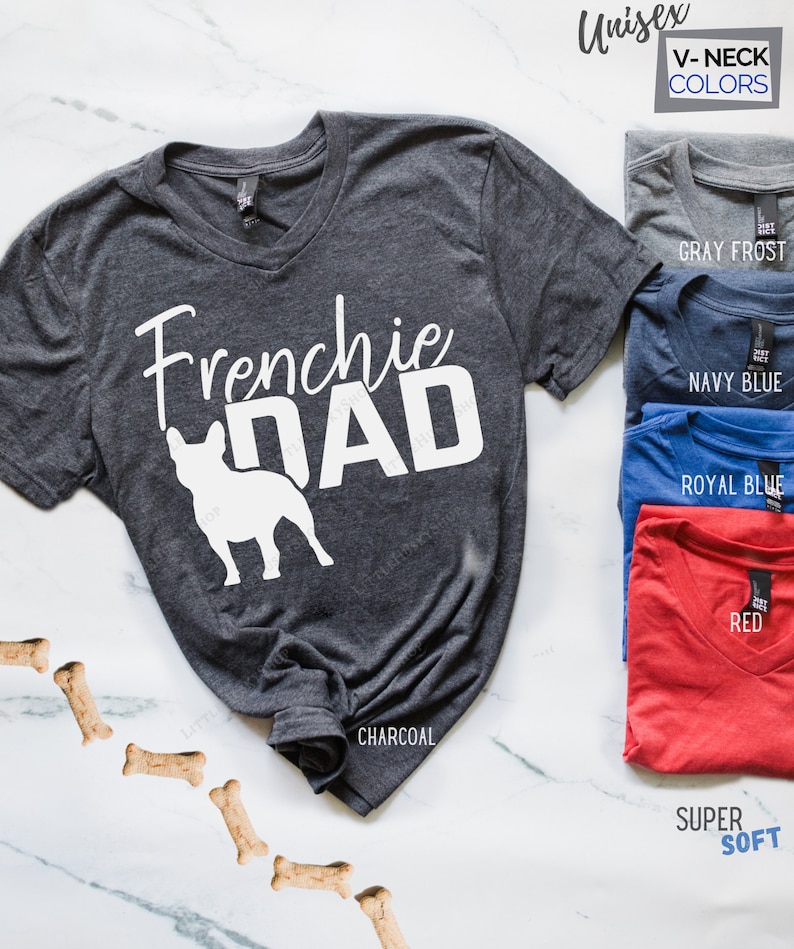 May include: Charcoal gray unisex V-neck t-shirt with the text "Frenchie DAD" and a white French Bulldog silhouette. Additional color options include Gray Frost, Navy Blue, Royal Blue, and Red. The shirt is labeled as Super Soft.
