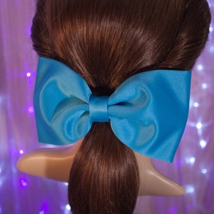 May include: A large, bright blue satin bow tied in a simple knot. The bow is tied around a ponytail of brown hair.