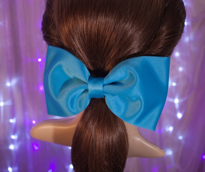May include: A large, bright blue satin bow tied in a simple knot. The bow is tied around a ponytail of brown hair.