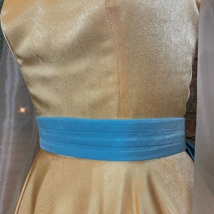 May include: A gold satin dress with a blue velvet sash. The dress has a fitted bodice and a full skirt.