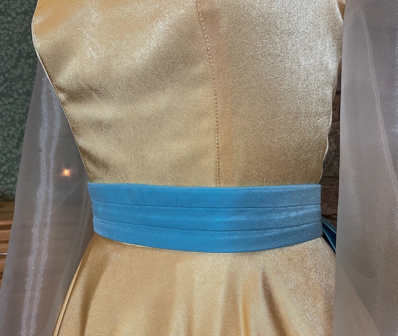 May include: A gold satin dress with a blue velvet sash. The dress has a fitted bodice and a full skirt.