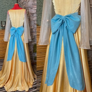 May include: A yellow satin gown with a large blue satin bow at the waist. The gown has sheer, white sleeves.