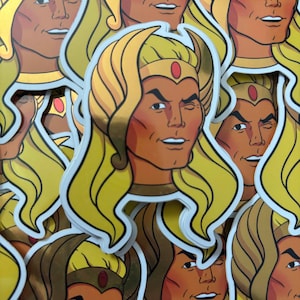 May include: A stack of gold foil stickers featuring a cartoon character with long blonde hair, a gold crown, and a winking expression. The character has a tan complexion and is wearing a red jewel on their forehead.