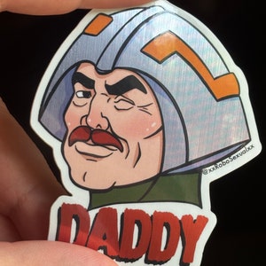May include: A sticker featuring a cartoon character with a mustache and a helmet. The character is winking and the sticker says "Daddy" in red letters.