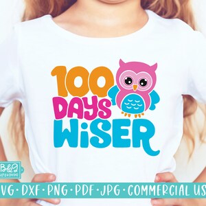 May include: A white t-shirt with the text "100 Days Wiser" in colorful letters. A pink owl with blue wings is next to the text.