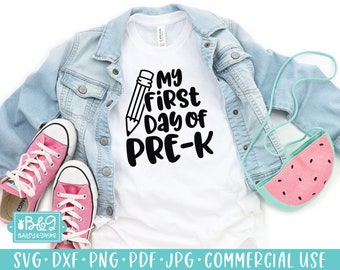 May include: White t-shirt with black text that reads "My First Day of Pre-K" with a black pencil graphic. The shirt is laying on a blue denim jacket and pink sneakers.