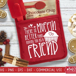 May include: Red oven mitt with a white design that says "There is muffin better than having you as a friend". The oven mitt is on a white wooden background with gingerbread cookies and other festive decorations.