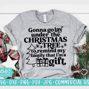 May include: A gray t-shirt with a Christmas tree design and the text "Gonna go lay under the Christmas Tree to remind my family that I'm a gift".