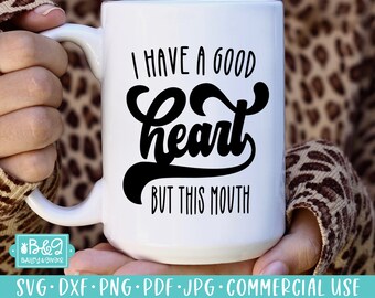 May include: A white ceramic mug with the black text "I HAVE A GOOD heart BUT THIS MOUTH". The mug has a large handle and is held by a person wearing a leopard print sweater. The mug is a standard size for tea or coffee.