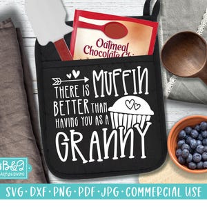 Może przedstawiać: Czarny rękawica kuchenna z napisem "There is muffin better than having you as a granny". W kieszeni znajduje się opakowanie mieszanki płatków owsianych z kawałkami czekolady i szpatułka. W pobliżu znajduje się drewniana łyżka i miska z jagodami.