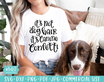 May include: White t-shirt with black text that reads "It's not dog hair it's canine confetti!" A brown and white dog is sitting next to the person wearing the shirt.