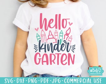 Könnte beinhalten: Weißes T-Shirt mit den Worten "hello kinder GARTEN" in Pink und Türkis, mit Illustrationen von Buntstiften, Bleistiften und Kleber. Das T-Shirt ist für Kindergartenkinder.