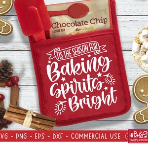 May include: Red oven mitt with the text "'Tis the season for baking spirits bright" in white. The oven mitt has a pocket on the front with a package of chocolate chip cookie mix inside.