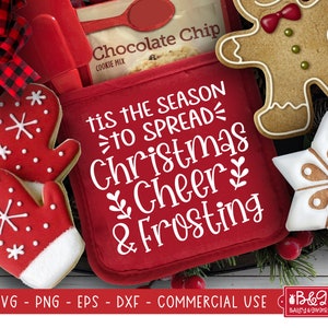 May include: Red pot holder with the text "Tis the season to spread Christmas cheer & frosting" in white. The pot holder is surrounded by gingerbread cookies, including a gingerbread man, a snowflake, and a mitten.