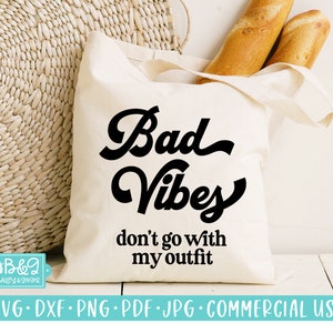 Puede incluir: Una bolsa de tela blanca con texto negro que dice "Bad Vibes don't go with my outfit".