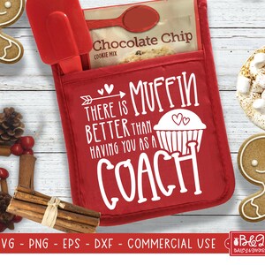 May include: A red oven mitt with the text "There is muffin better than having you as a coach" and a cupcake graphic. It contains a chocolate chip cookie mix and red spatula. The mitt is on a white wooden surface.