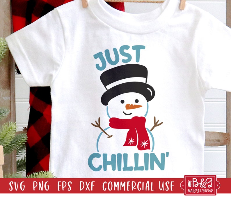 May include: White t-shirt with a snowman graphic. The snowman has a black top hat, a red scarf, and the text "JUST CHILLIN'" in blue. The shirt is hanging on a clothesline.