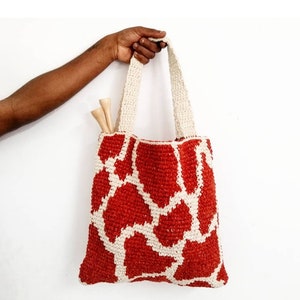 Puede incluir: Una bolsa de mano de crochet roja y blanca con estampado de jirafa. La bolsa tiene dos asas de color crema.