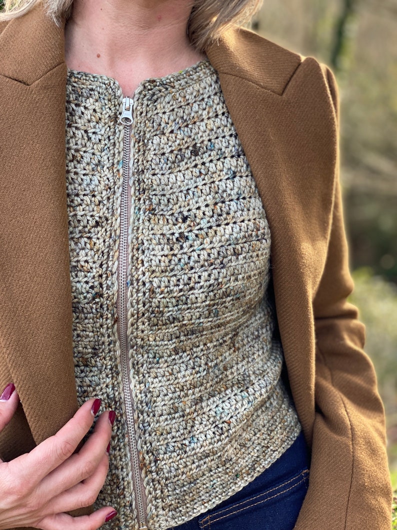 May include: A close-up of a brown crocheted top with a zip fastening. The top is worn over a blue denim shirt.