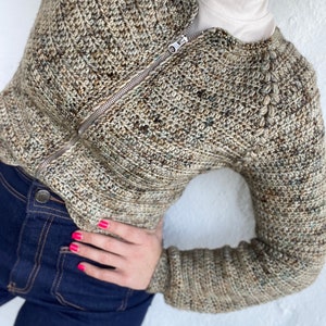 May include: A brown and beige crocheted cardigan with a zip closure. The cardigan has a textured stitch pattern and a high neckline.