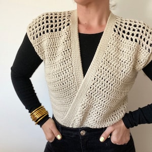 Op de afbeelding: Een beige gebreide vest zonder mouwen met een V-hals. Het vest is gemaakt met een eenvoudig steekpatroon en heeft een ontspannen pasvorm.