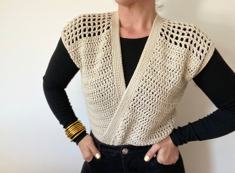 Op de afbeelding: Een beige gebreide vest zonder mouwen met een V-hals. Het vest is gemaakt met een eenvoudig steekpatroon en heeft een ontspannen pasvorm.