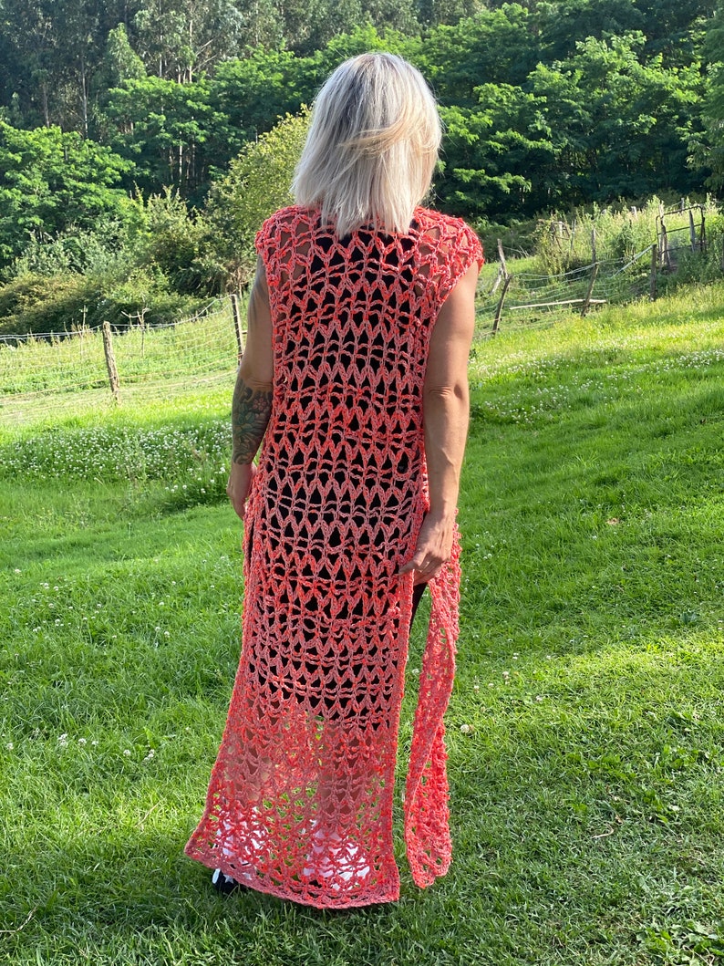 Pu&ograve; includere: Un lungo gilet in crochet color corallo con un delicato motivo a punto traforato. Il gilet ha una profonda scollatura a V e una silhouette lunga e fluida.