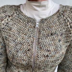 May include: A brown, green and white crocheted cardigan with a zip fastening. The cardigan has a textured stitch pattern and a round neckline.