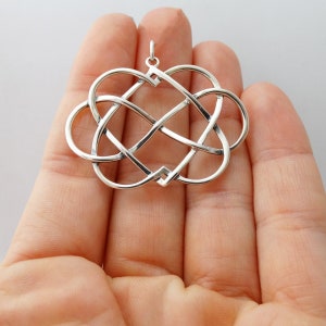 May include: A silver pendant in the shape of two intertwined hearts. The hearts are connected in a Celtic knot design.