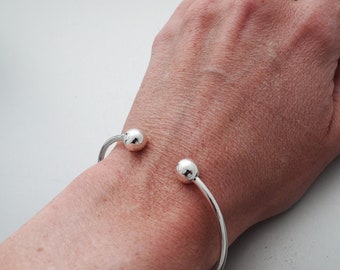 May include: A silver bangle bracelet with two round balls at the ends.