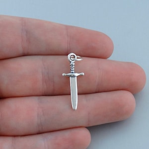May include: A silver sword charm with a detailed handle and a pointed tip.