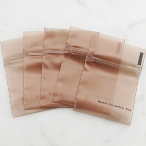 May include: Five brown plastic bags with a zipper closure. The bag on the bottom has the text "Tarnish Prevention Bag" printed on it.