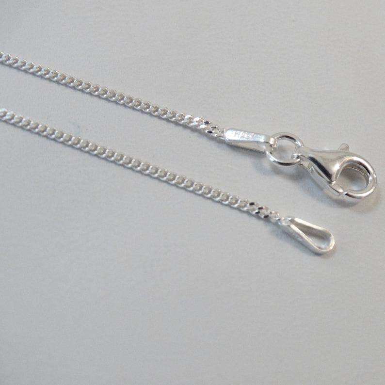 Puede incluir: Un collar de cadena de plata con un cierre de langosta y un anillo de salto. La cadena es de estilo curb.