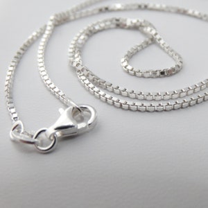 May include: A silver chain necklace with a box clasp. The chain is made of small, square links.