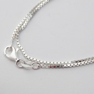 May include: A silver chain necklace with a box chain design. The chain is layered and has a lobster claw clasp.