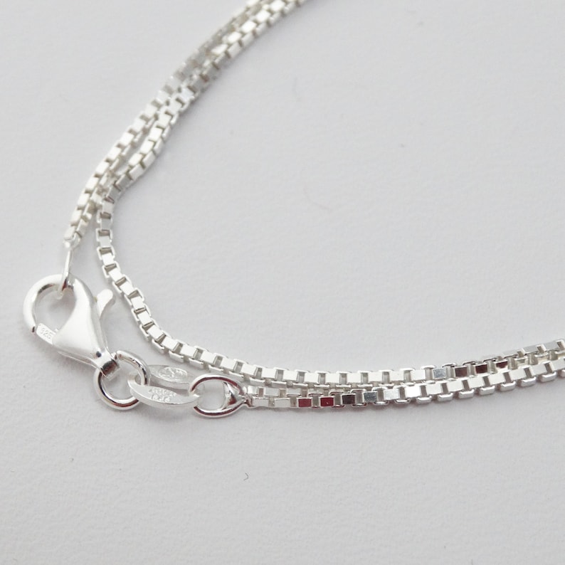 May include: A silver chain necklace with a box chain design. The chain is layered and has a lobster claw clasp.