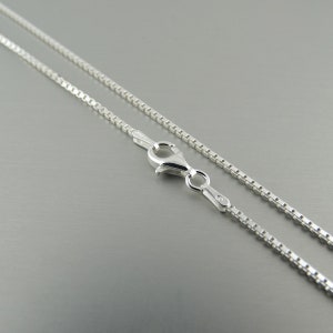 May include: A silver chain necklace with a lobster clasp fastening. The chain is made of small, square links.