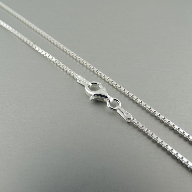 May include: A silver chain necklace with a lobster clasp fastening. The chain is made of small, square links.