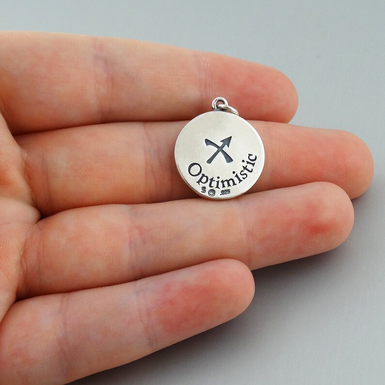 May include: Silver charm with a Sagittarius zodiac symbol and the word "Optimistic" engraved on it.