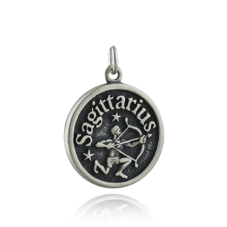 May include: Silver charm pendant featuring the Sagittarius zodiac sign. The charm is round and has a black background with a silver image of a centaur holding a bow and arrow. The word "Sagittarius" is written around the edge of the charm.