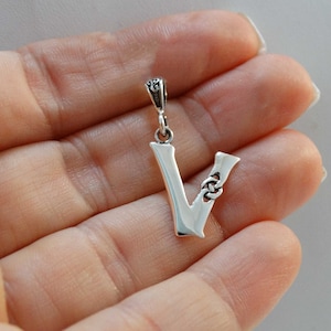 May include: A silver pendant in the shape of the letter V with a Celtic knot design. The pendant is on a white background.