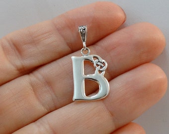 Puede incluir: Pendiente de plata con la letra B y un diseño de nudo celta. El pendiente está sobre un fondo blanco.