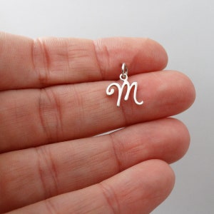 May include: Silver charm with a cursive letter M.