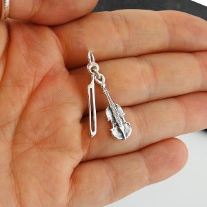 May include: Silver charm featuring a violin and bow. The charm is detailed and has a realistic design.