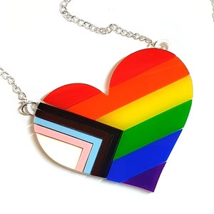 May include: A silver chain necklace with a rainbow heart pendant. The heart is made of layered acrylic and features the colours of the pride flag.