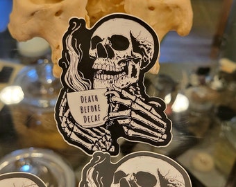 May include: Black and white sticker of a skeleton holding a coffee mug that says "Death Before Decaf".