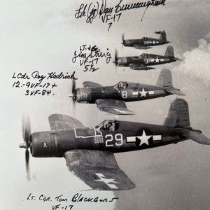 May include: Black and white photo of four fighter planes in formation. The planes are all Vought F4U Corsairs, and they are flying in a tight formation. The planes are all numbered, and the numbers are visible in the photo. The photo is signed by several of the pilots, including Lt. Cdr. Tom Blackburn, VF-17.