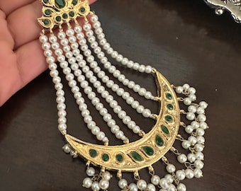 May include: A gold and green jeweled pendant with a crescent moon design and multiple strands of white pearls.